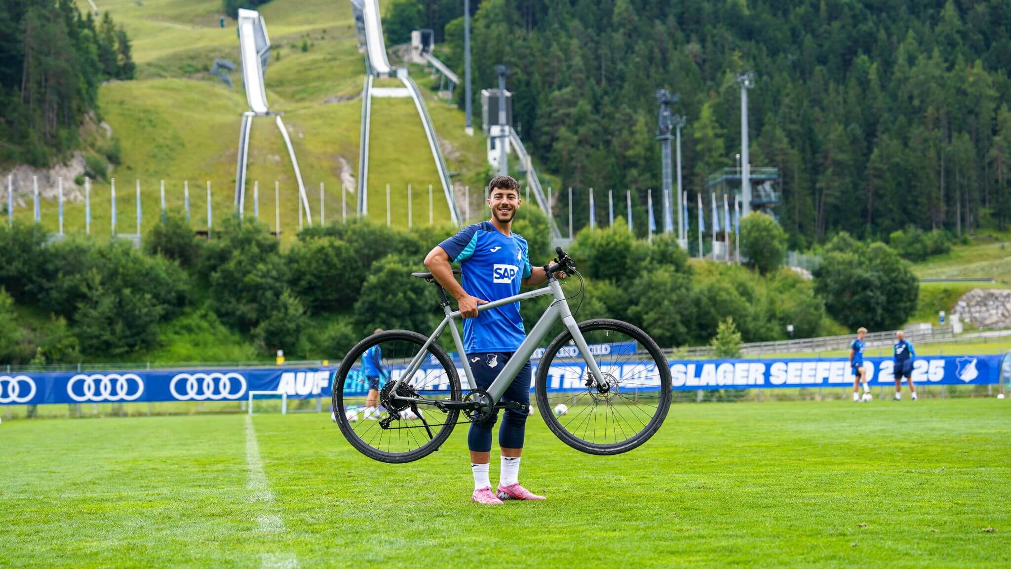 Hoffenheim Spieler steht auf Rasen und hebt Coboc E-Bike hoch